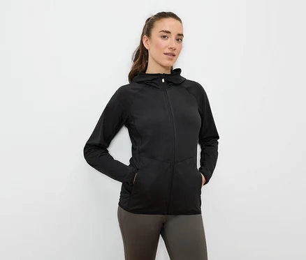 Žena má ruce v kapsách černé sportovní bundy s kapucí na zip.