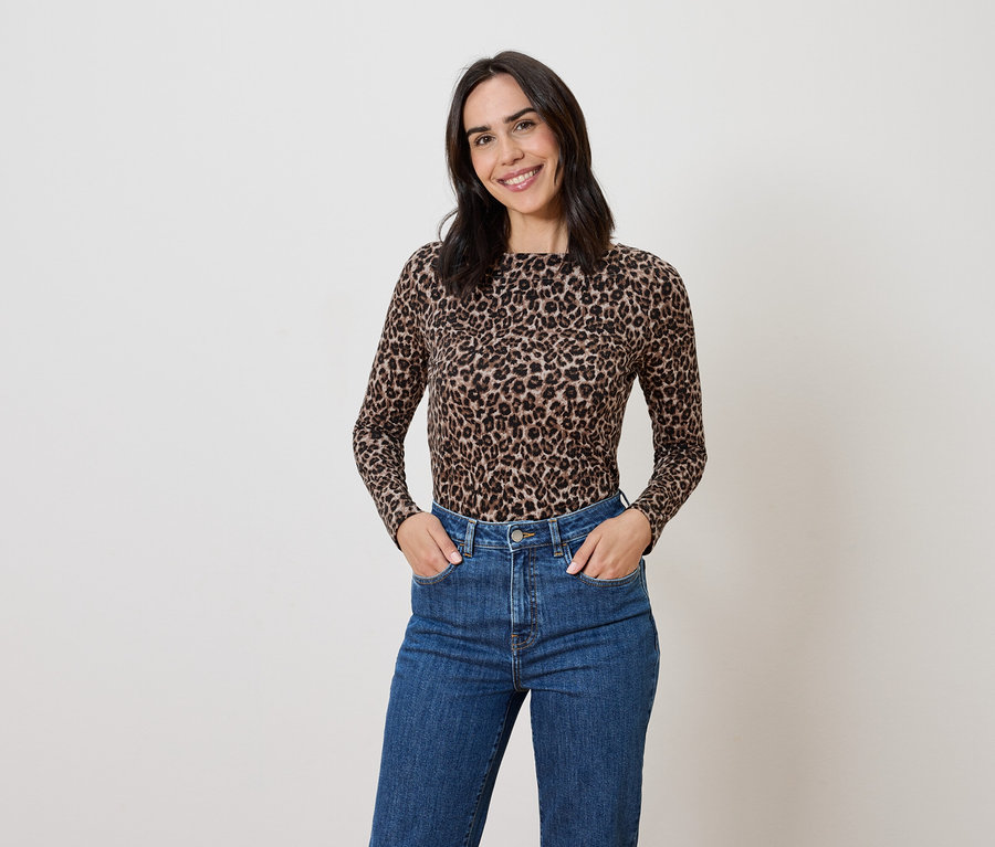 Žena s hnědými vlasy pózuje v topu se zvířecím potiskem a modrých džínách.