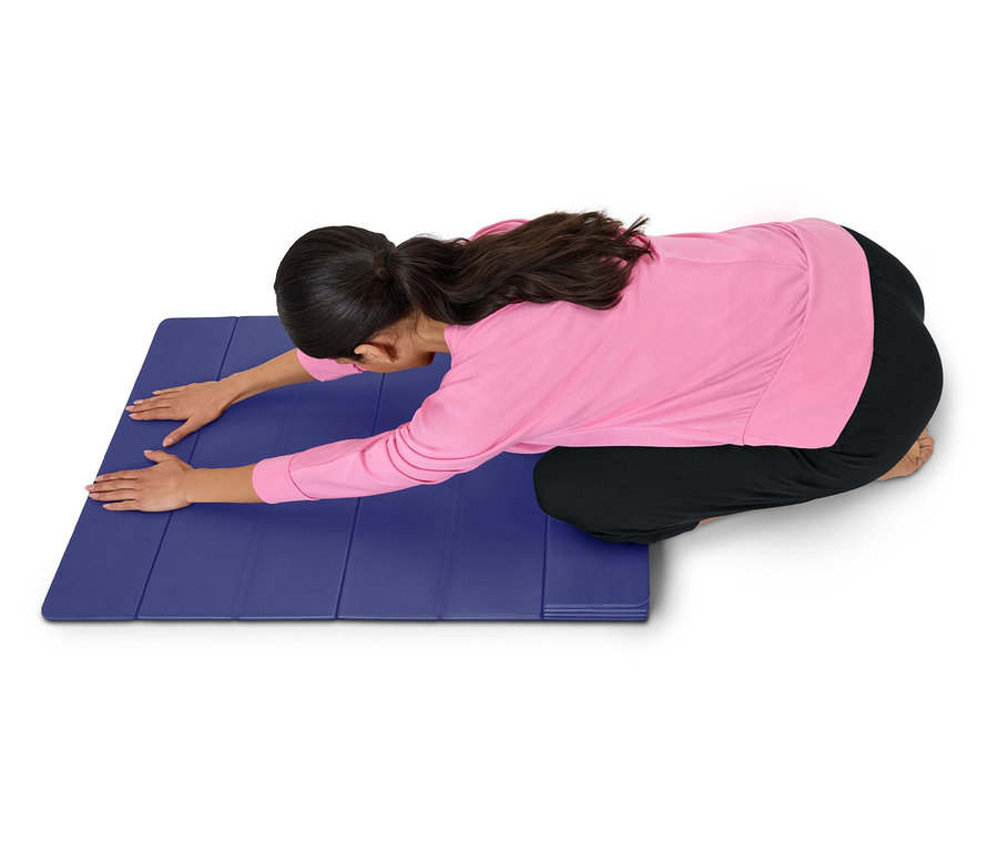 Žena v růžovém topu a černých kalhotách se protahuje na modré podložce.