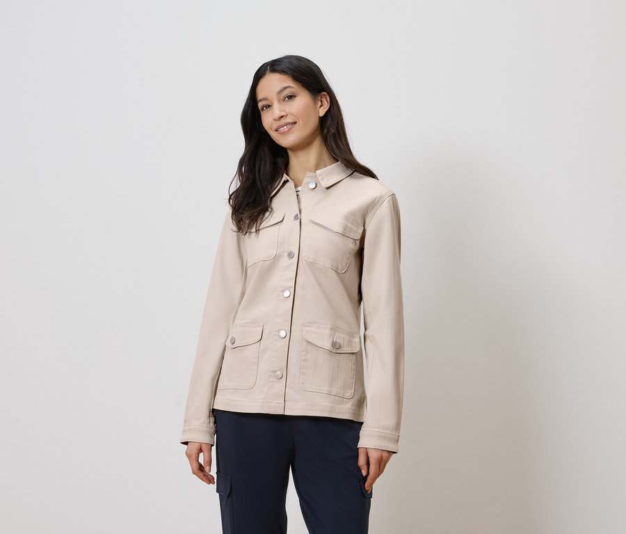 Žena má na sobě béžovou bundu a modré kalhoty.