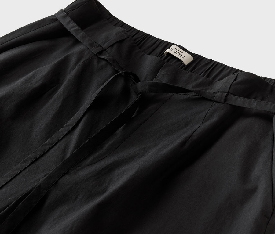 Detailní záběr na černé kalhoty se zavazovacím páskem a štítkem s nápisem "TCHINO MY STYLE".