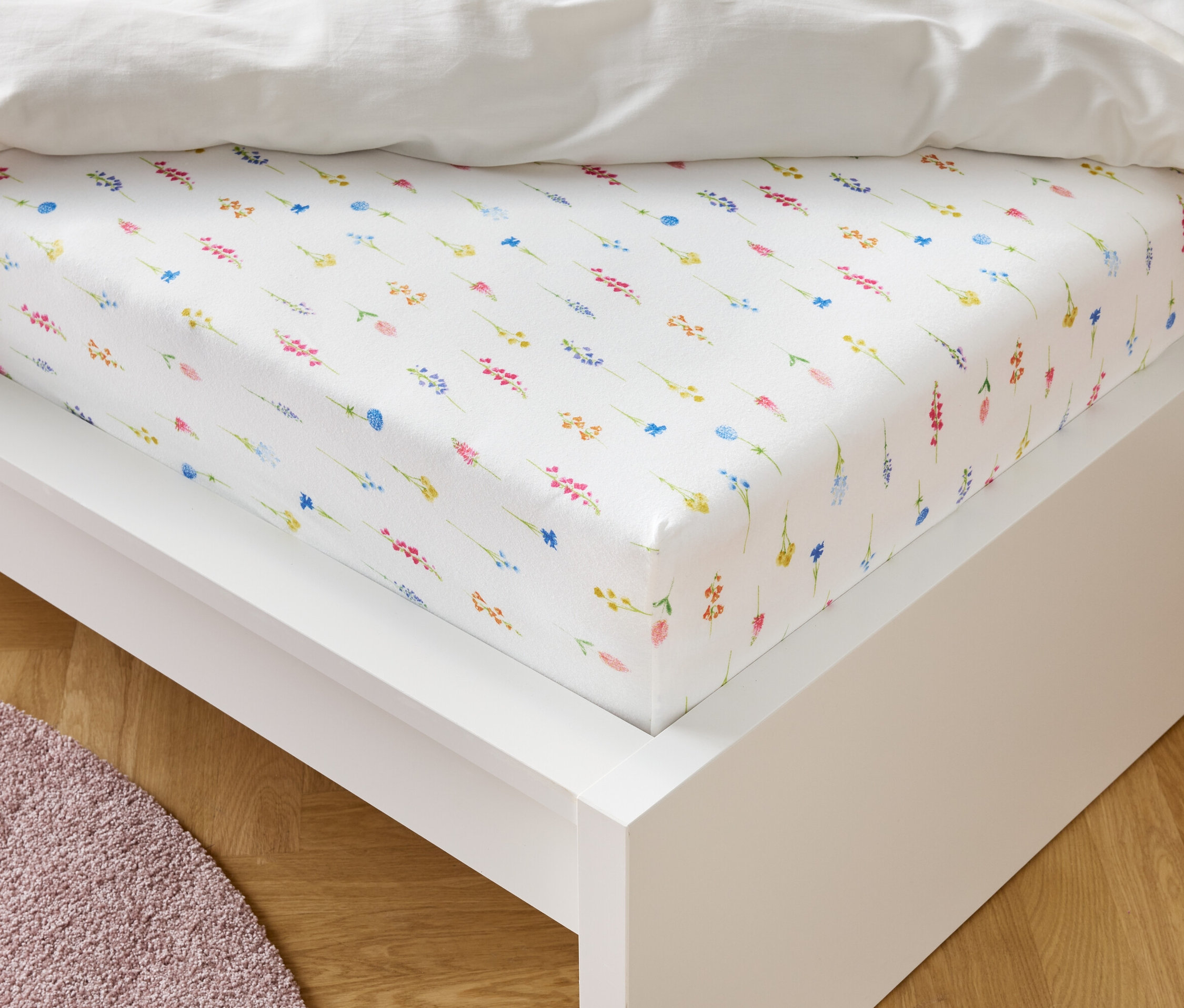 Bílé prostěradlo s květinovým vzorem leží na bílém rámu postele.