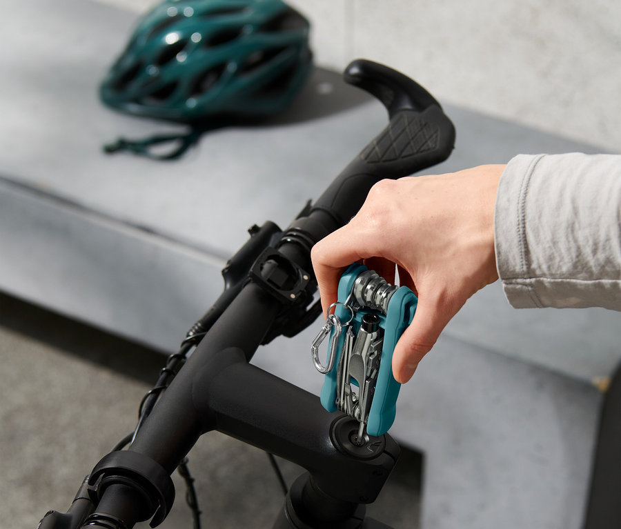 Ruka připevňuje multifunkční nástroj na řídítka kola, v pozadí cyklistická helma.