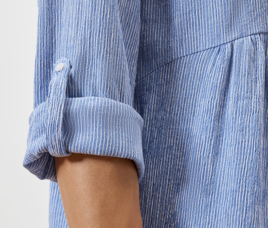 Detail ohrnutého rukávu modrobílé pruhované košile.