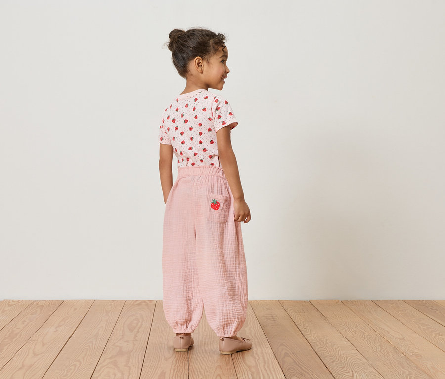 Dívka zezadu, má na sobě jahodové tričko a růžové kalhoty s jahodovým detailem.