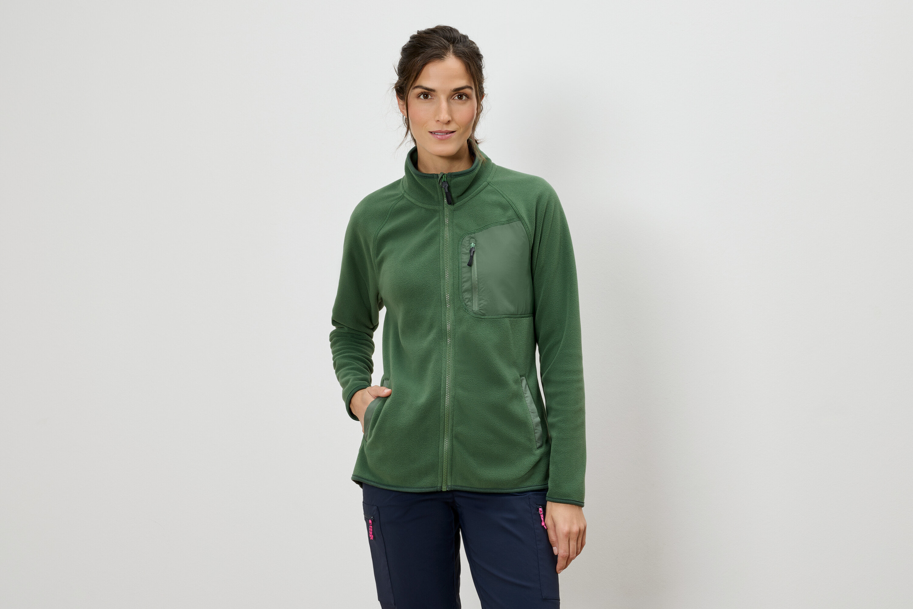 Žena v zelené fleecové bundě na zip a modrých kalhotách.