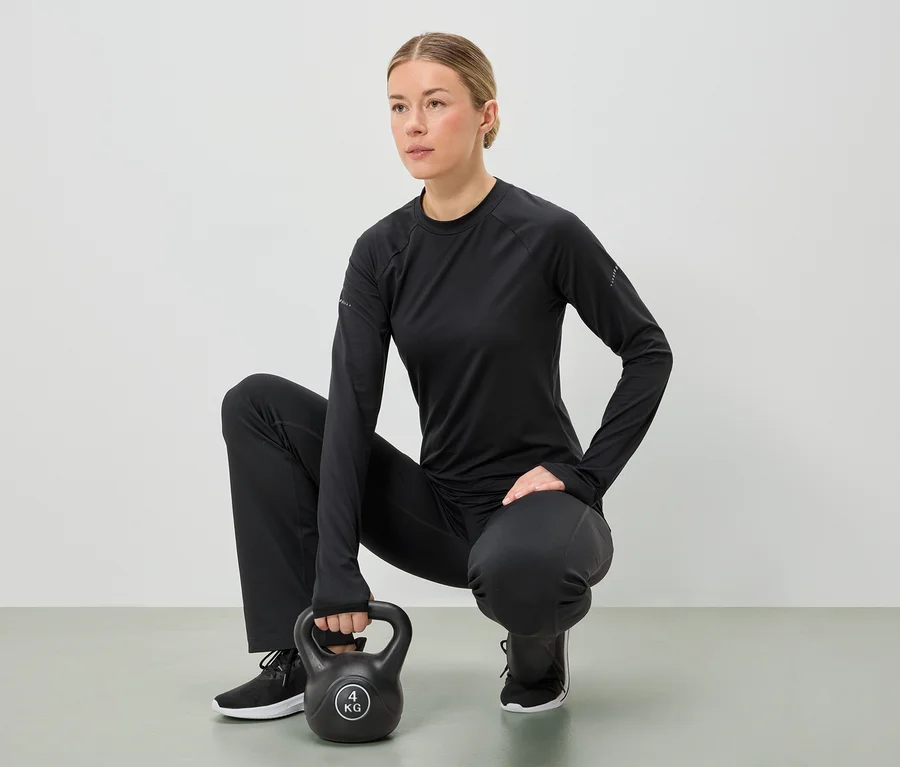 Žena v černém sportovním oblečení dřepí a oběma rukama drží 4 kg kettlebell.