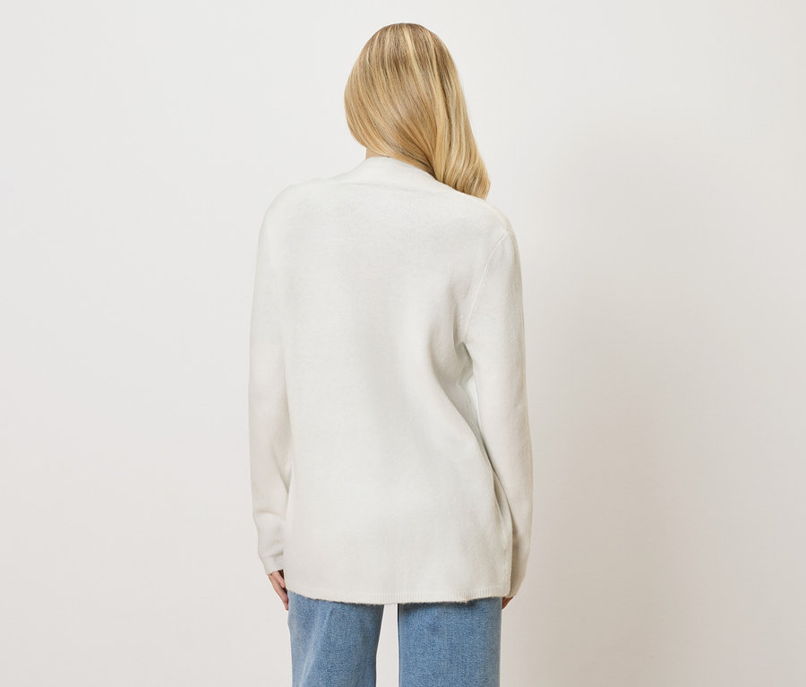 Pohled zezadu na ženu s blond vlasy v bílém kardiganu a džínách.