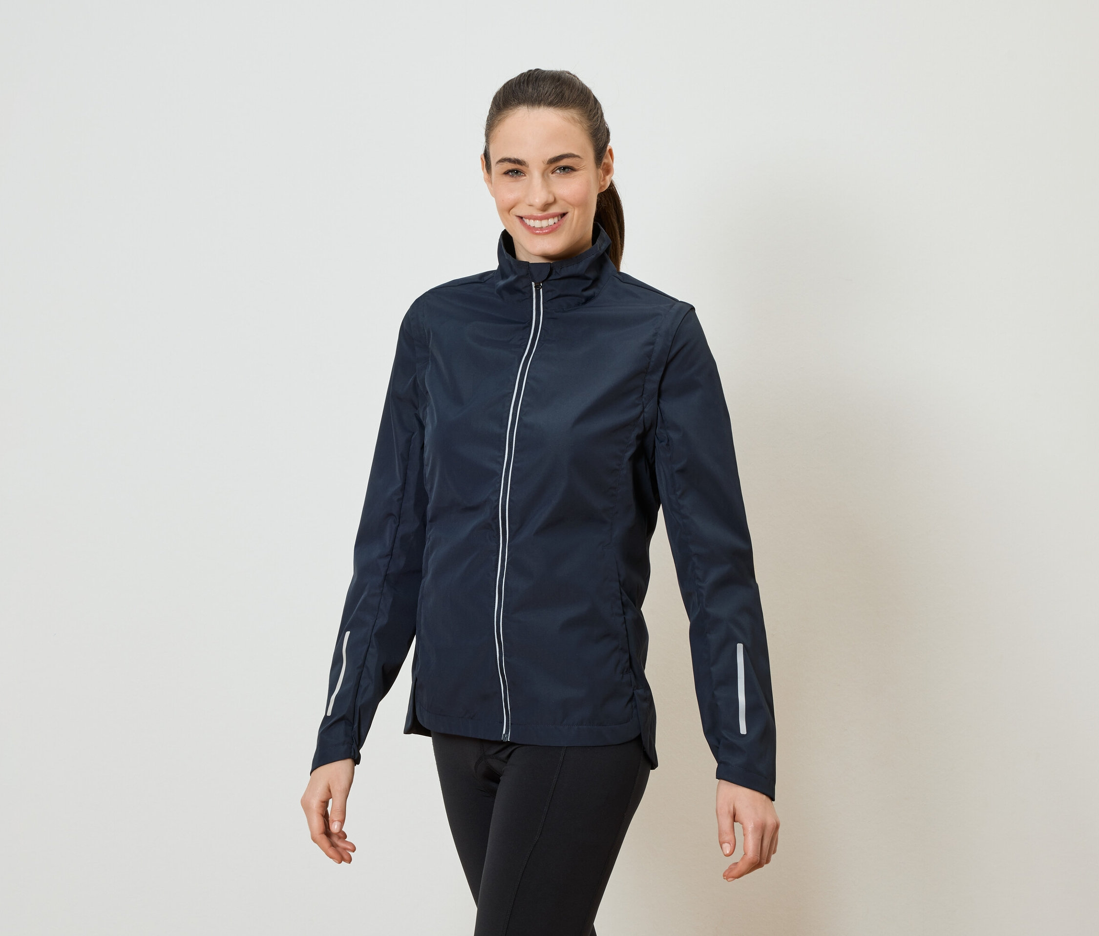 Žena s culíkem má na sobě tmavě modrou bundu na zip a černé legíny.