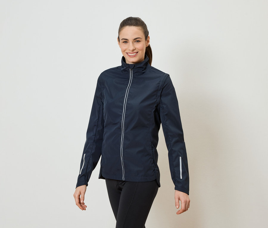 Žena s culíkem má na sobě tmavě modrou bundu na zip a černé legíny.