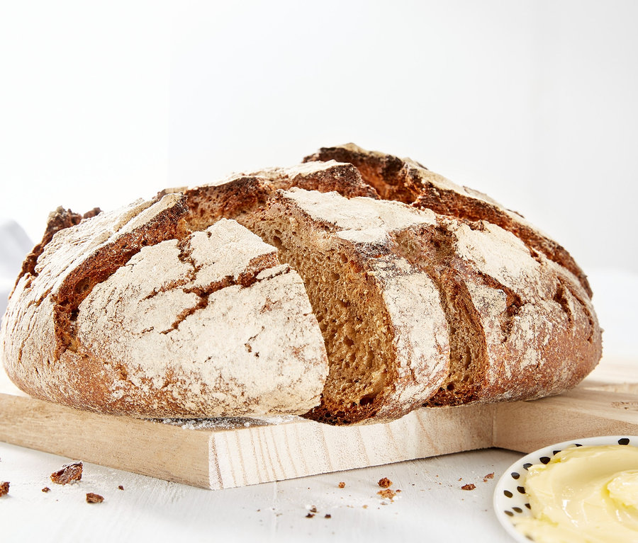 Bochník chleba na dřevěném prkénku vedle talíře másla.