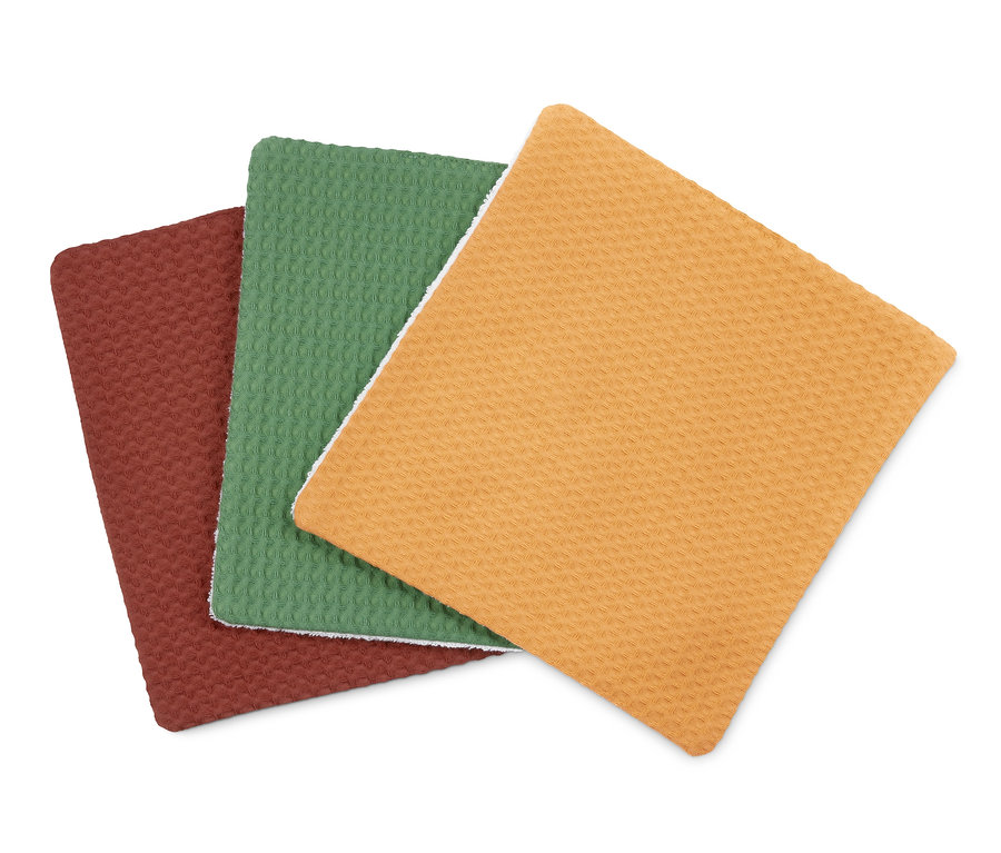 Tři hadříky na nádobí leží na sobě. Jsou barevné: bordó, zelené a žluté.