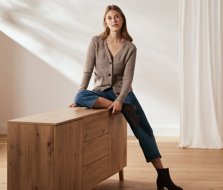 Žena sedí na komodě a má na sobě zkrácené džíny.