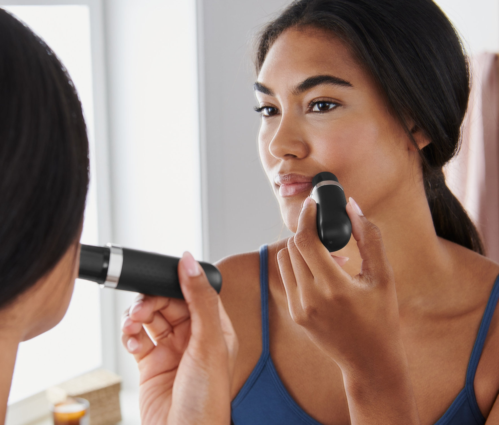 Žena používá elektrický depilátor na obličej před zrcadlem.
