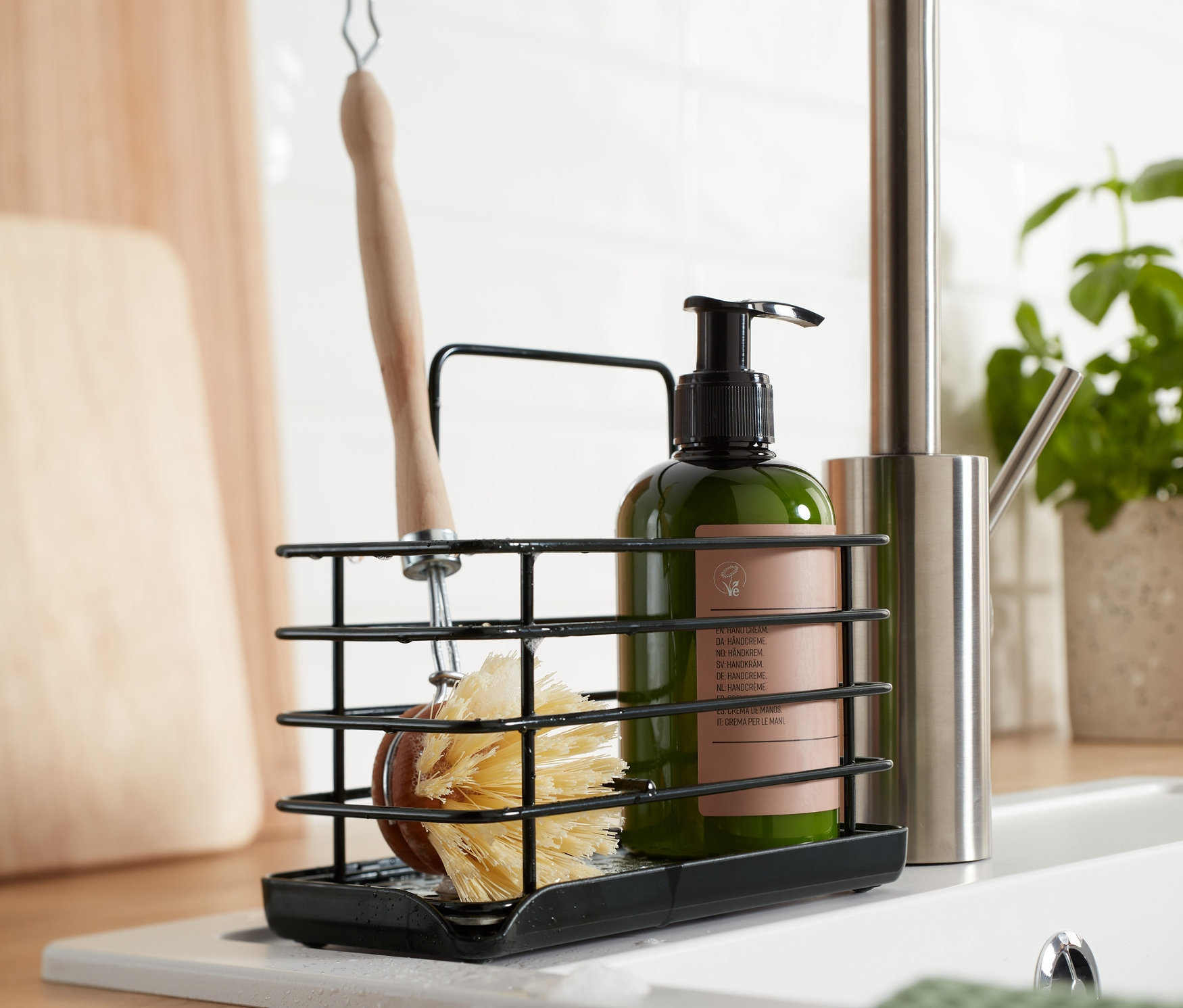 Černý kovový stojan na mycí potřeby s kartáčem a lahví mýdla na umyvadle.