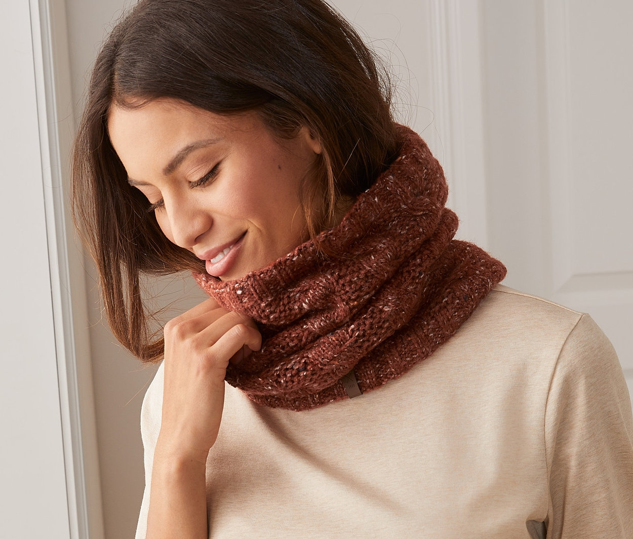 Žena si upravuje pletenou kruhovou šálu na krku.