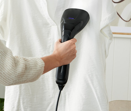 Žena používá napařovač na bílou košili visící na ramínku.