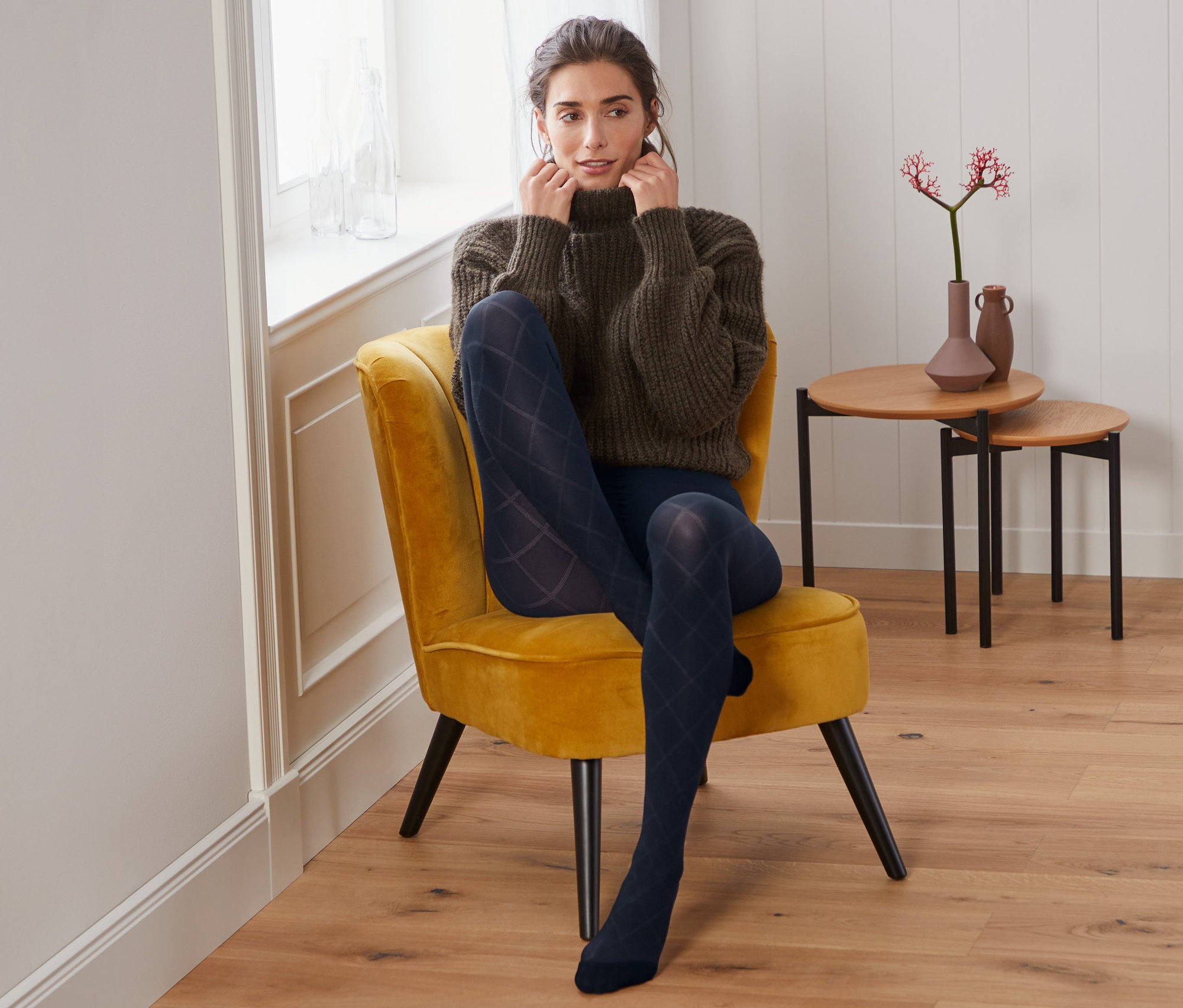 Žena sedí v křesle a má na sobě jemné punčochy s kostkovaným vzorem.