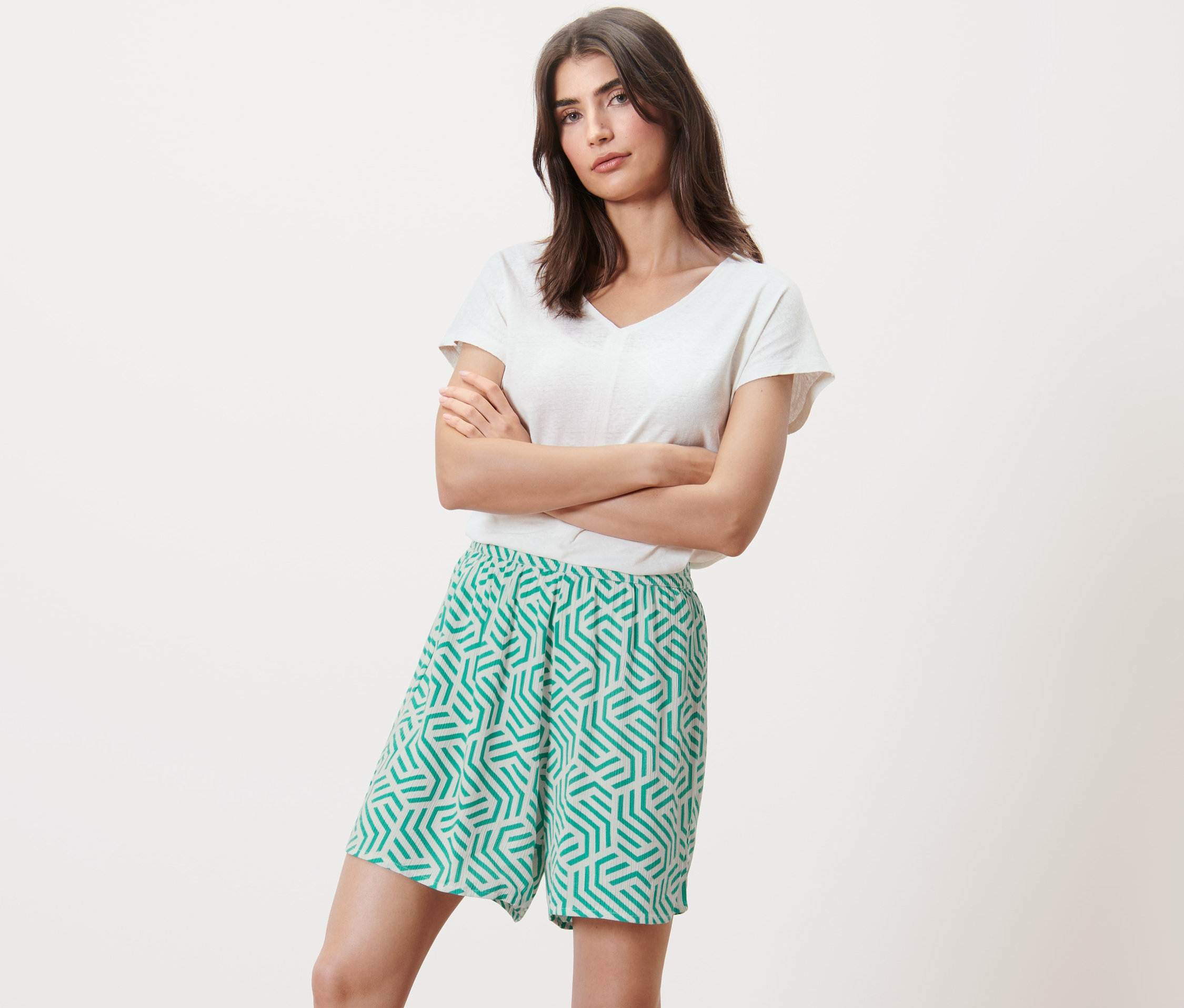 Žena se zkříženýma rukama pózuje v tkaných šortkách s potiskem.