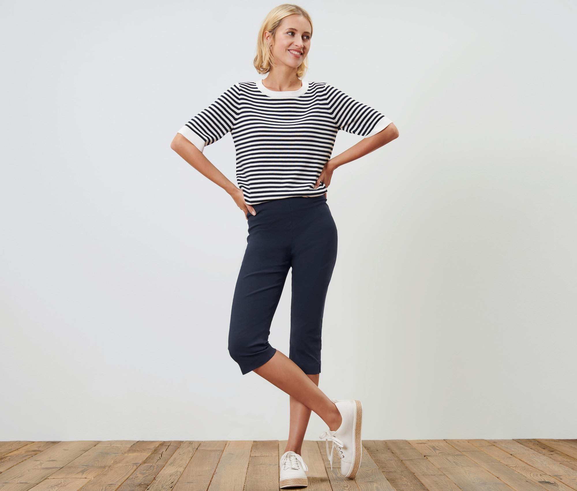 Žena pózuje v tmavě modrých 3/4 strečových kalhotách a pruhovaném topu.