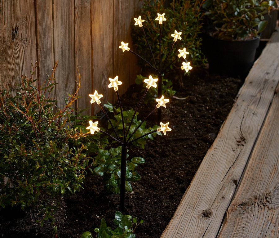 Dva LED bodce k zapíchnutí do země ve tvaru hvězdy, umístěné v záhonu u dřevěného plotu.