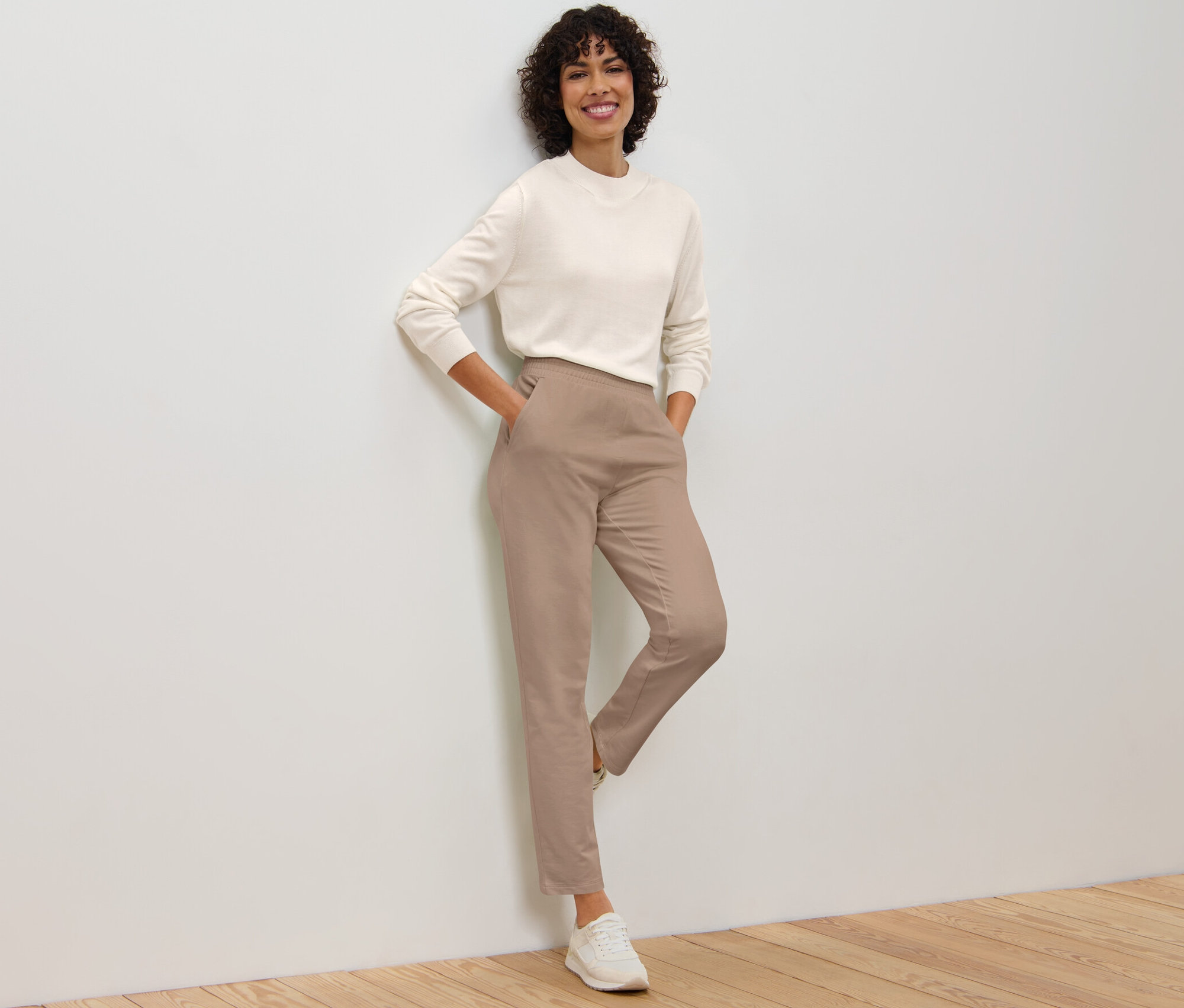 Žena opřená o zeď pózuje v béžových joggpantech.