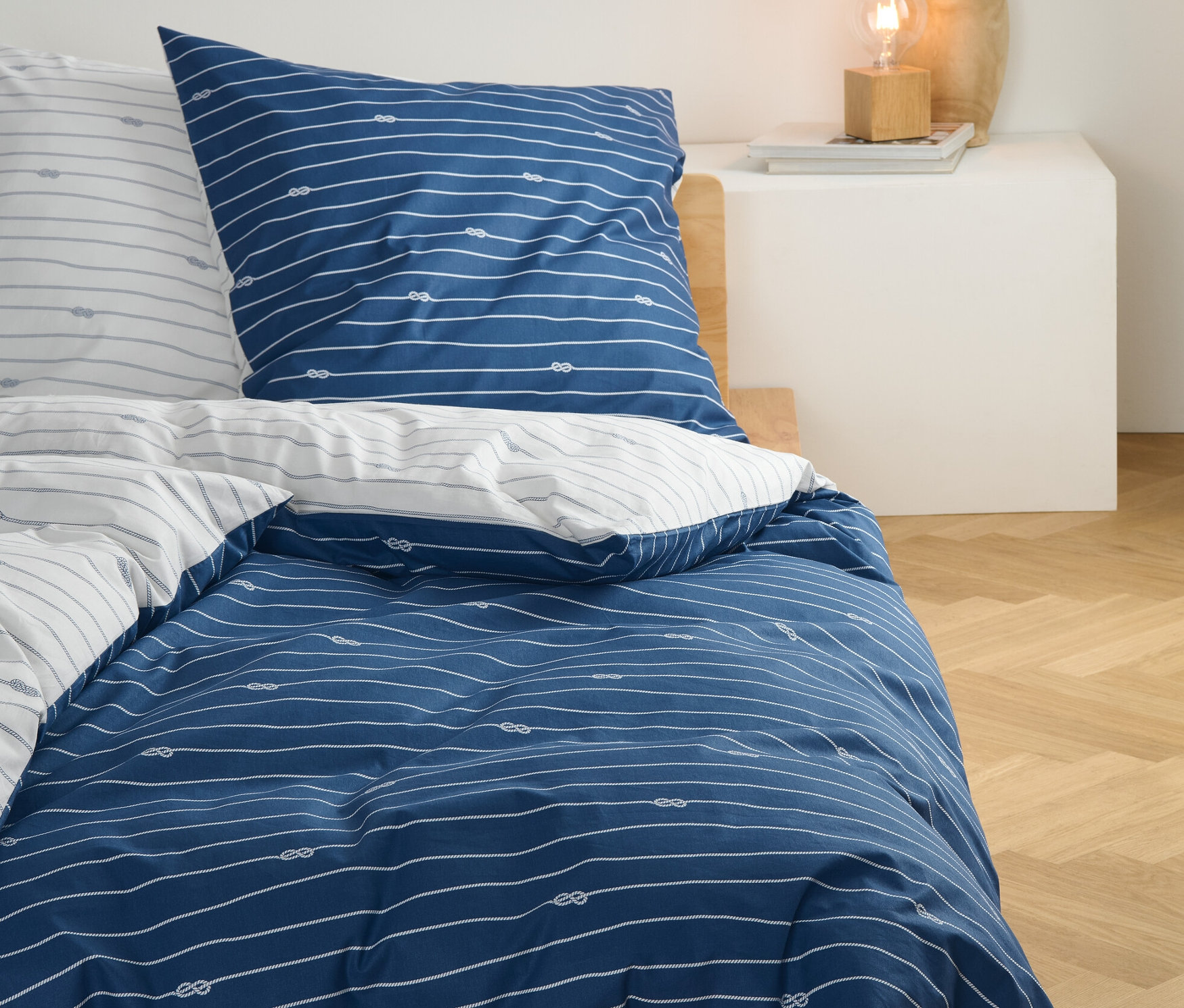 Modrá perkálová přikrývka standardní velikosti s bílými pruhy a vzorem uzlů na posteli.