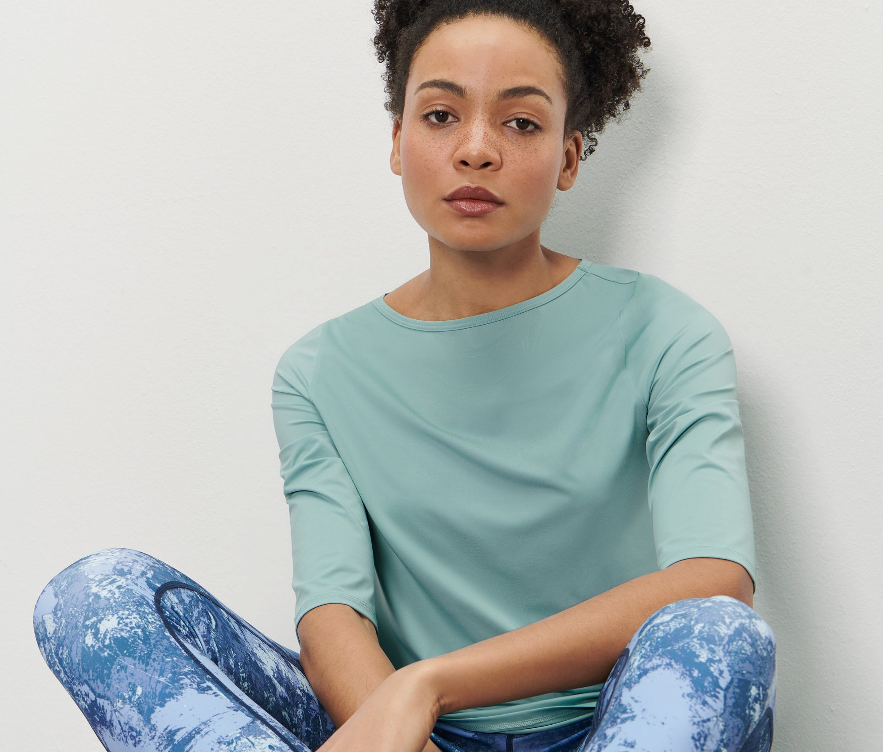 Žena sedí a má na sobě mátově zelené funkční triko s 3/4 rukávy.