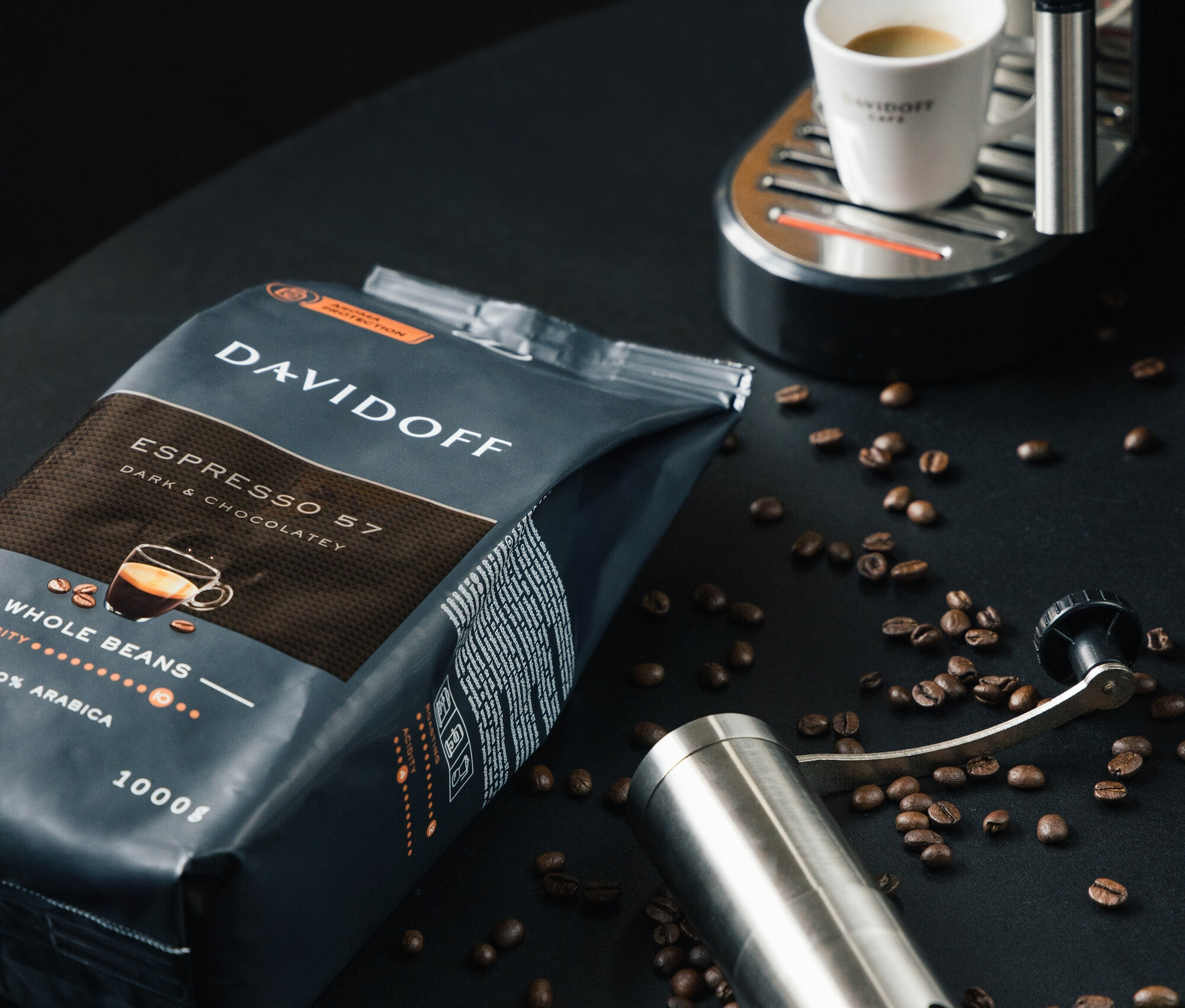 Balení zrnkové kávy DAVIDOFF CAFÉ Espresso 57 1000 g, mlýnek na kávu a šálek na espresso pod kávovarem.