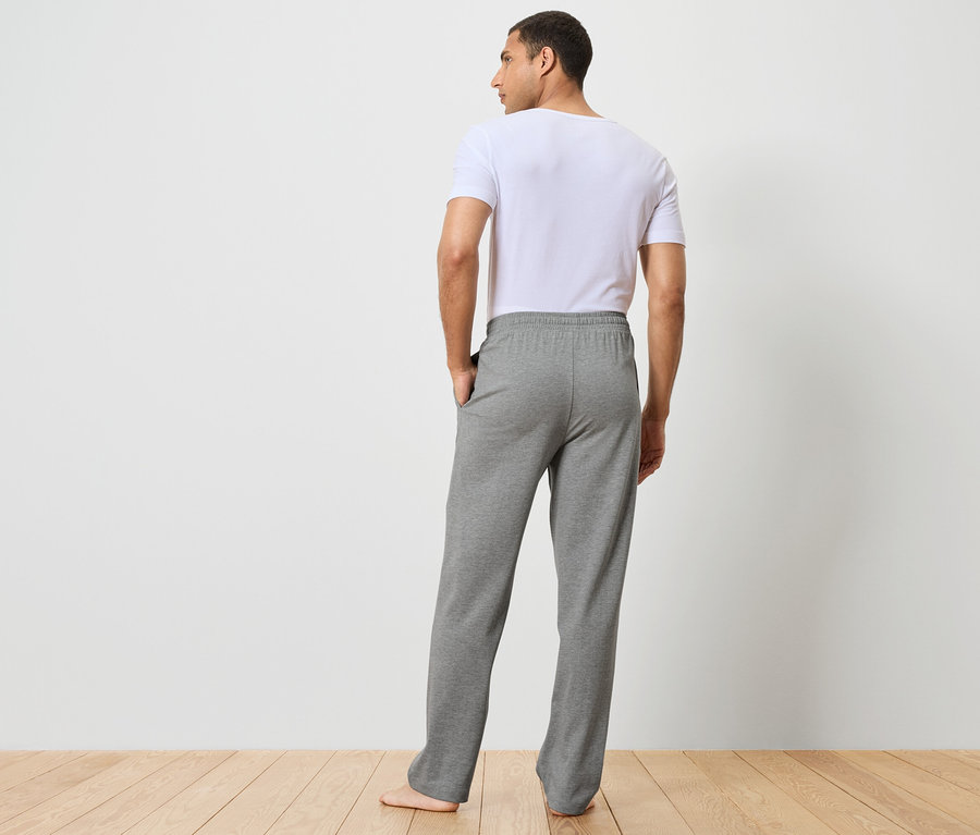 Muž zády k fotoaparátu má na sobě šedé tepláky a bílé tričko.