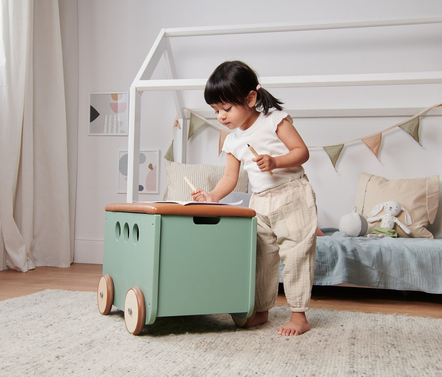 Dívka kreslí na stole, na sobě má béžové navlékací kalhoty z biobavlny.