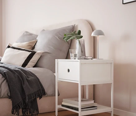 Šedá bateriová stolní lampa s LED na bílém nočním stolku vedle postele.