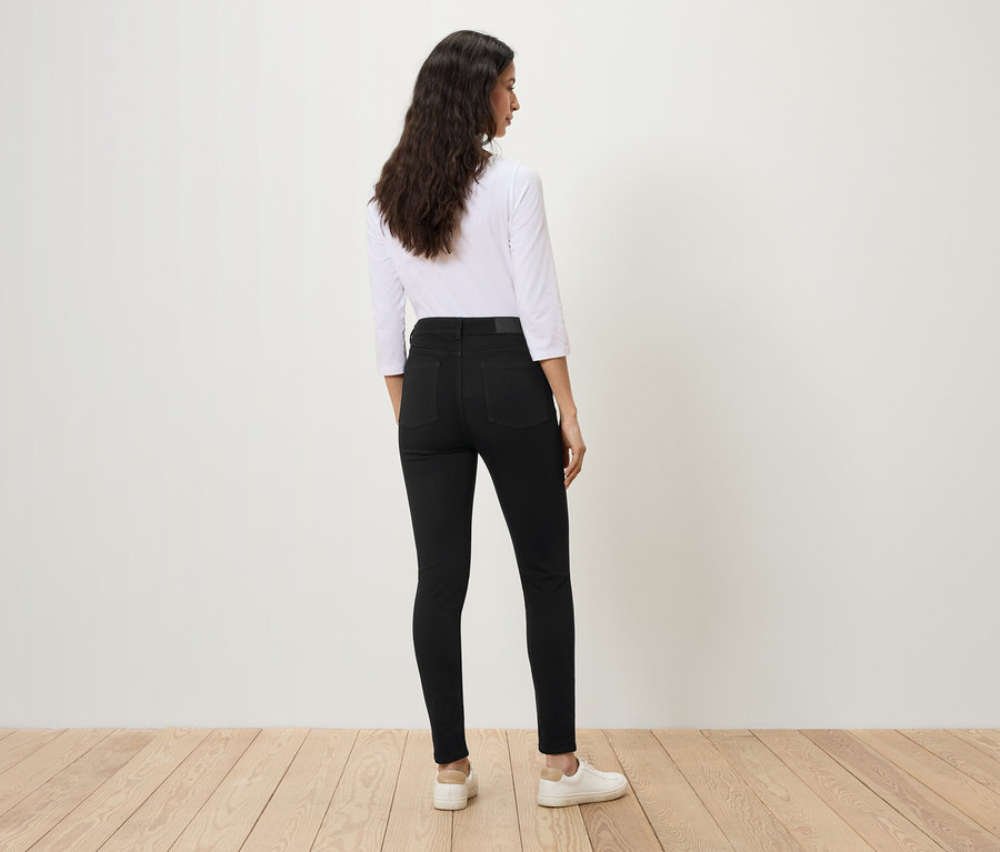 Žena stojí zády k fotoaparátu a má na sobě černé džíny a bílou košili.