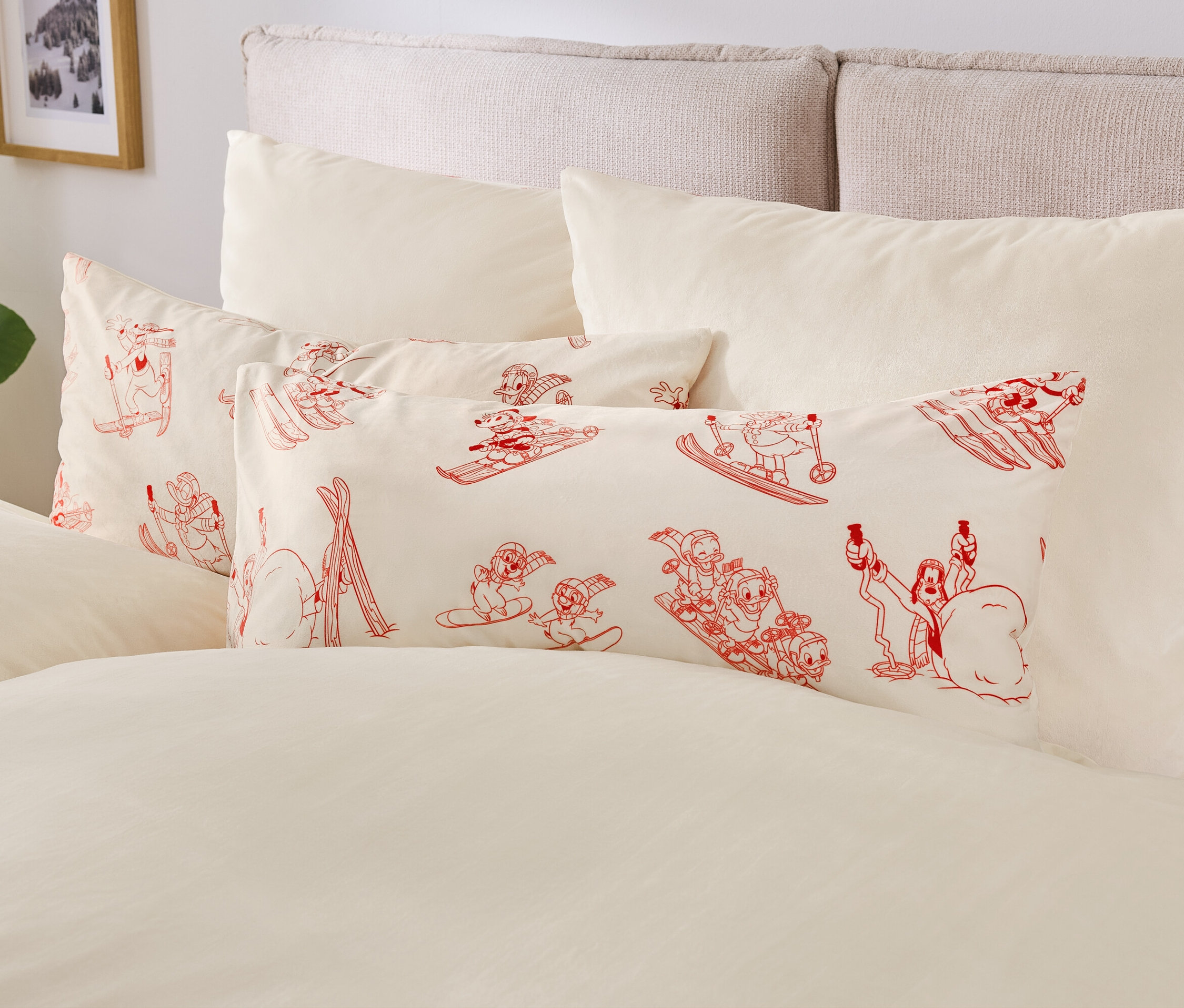 Béžové povlečení s polštáři s červenými kreslenými postavičkami na lyžích a snowboardech.