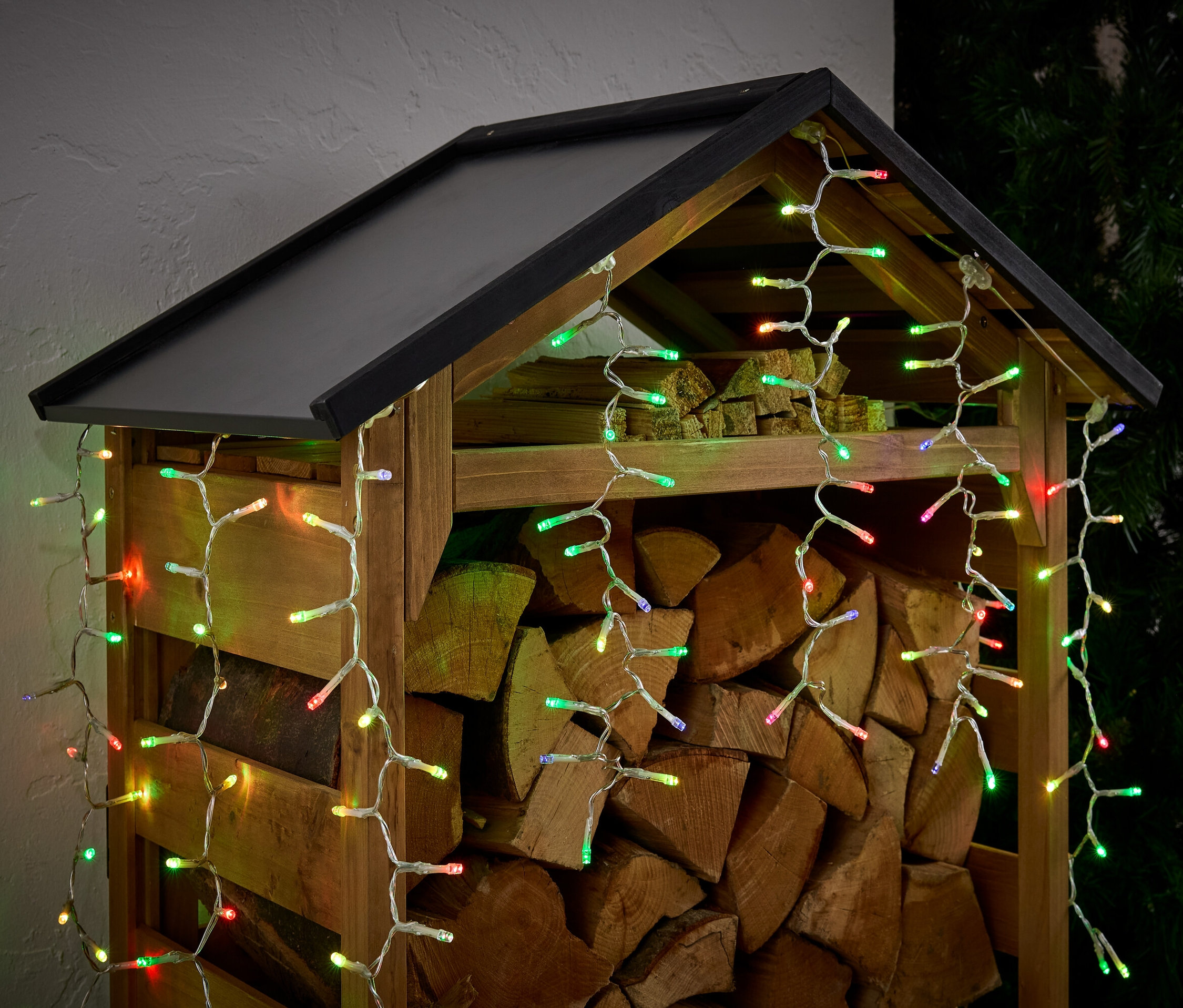 Dřevník plný dřeva, ozdobený barevnými světýlky.