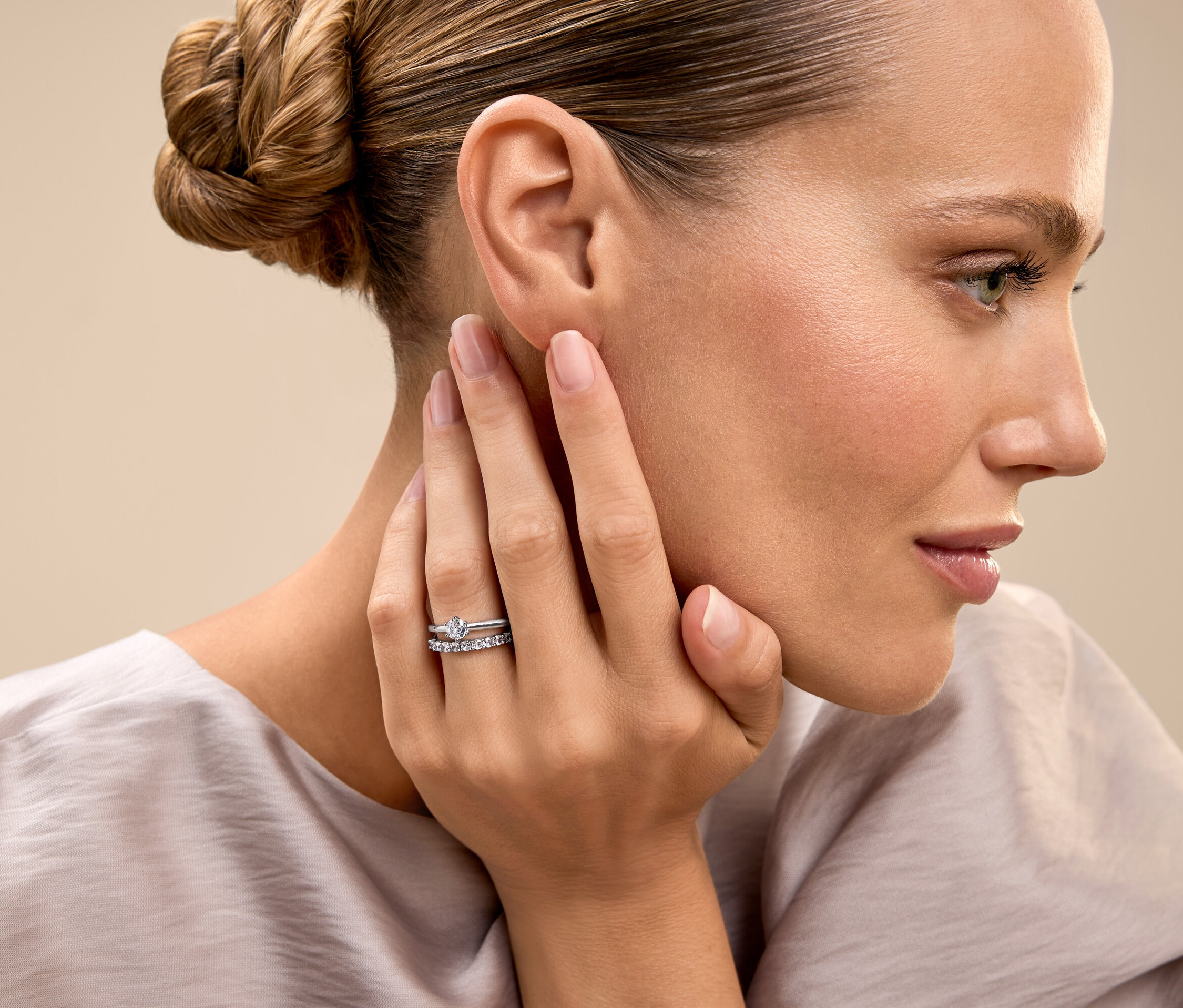 Žena se sepnutými vlasy se dotýká tváře a ukazuje prsten.