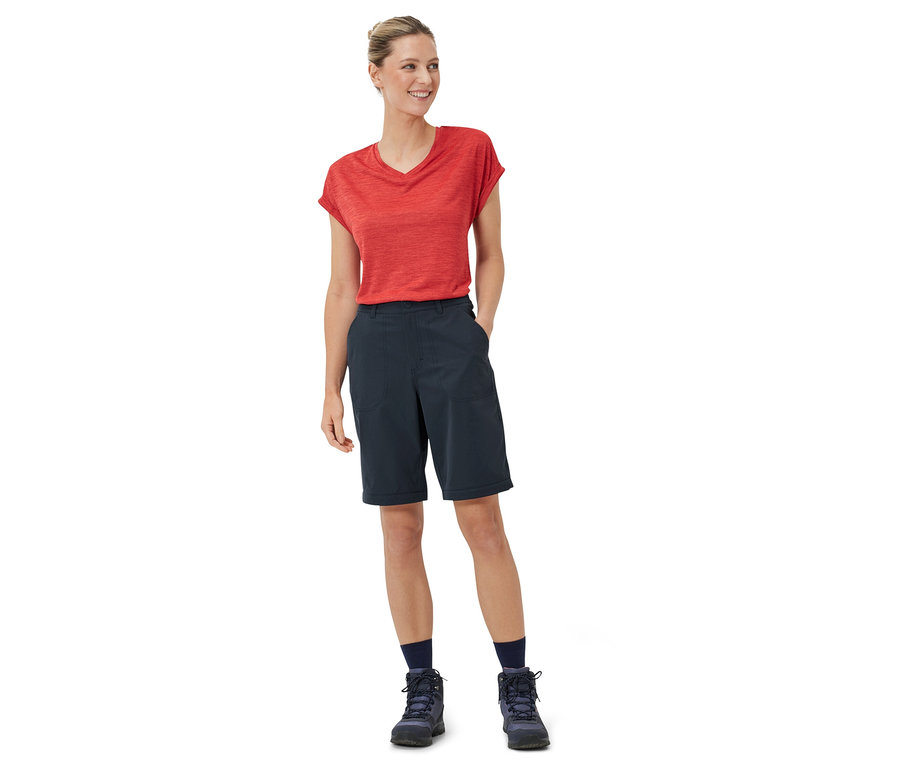 Žena stojí a má na sobě červené tričko a modré funkční kalhoty 2 v 1.