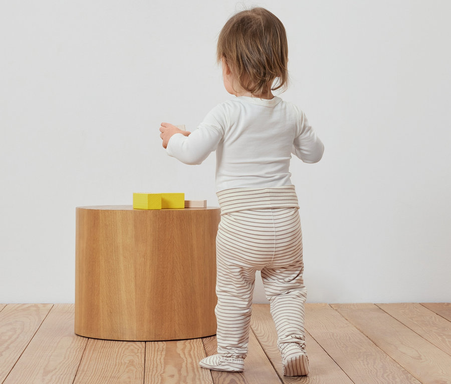 Batole stojí zády a hraje si s hračkami vedle 3 ks dupaček pro miminka.