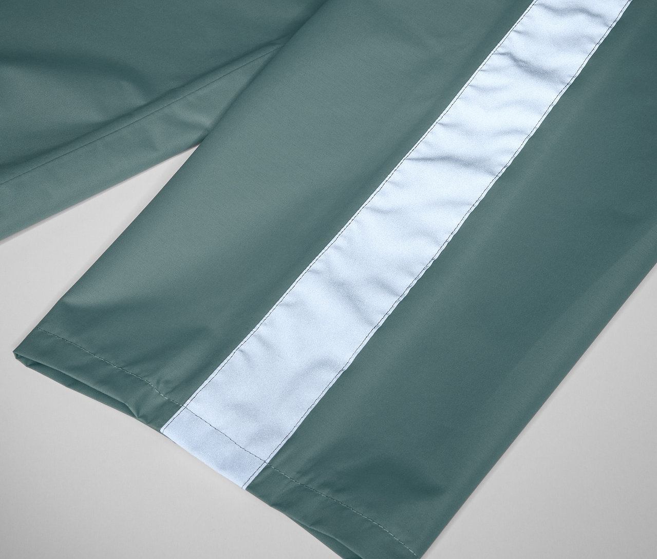 Detail dětských kalhot do deště šalvějové barvy s reflexním pruhem.