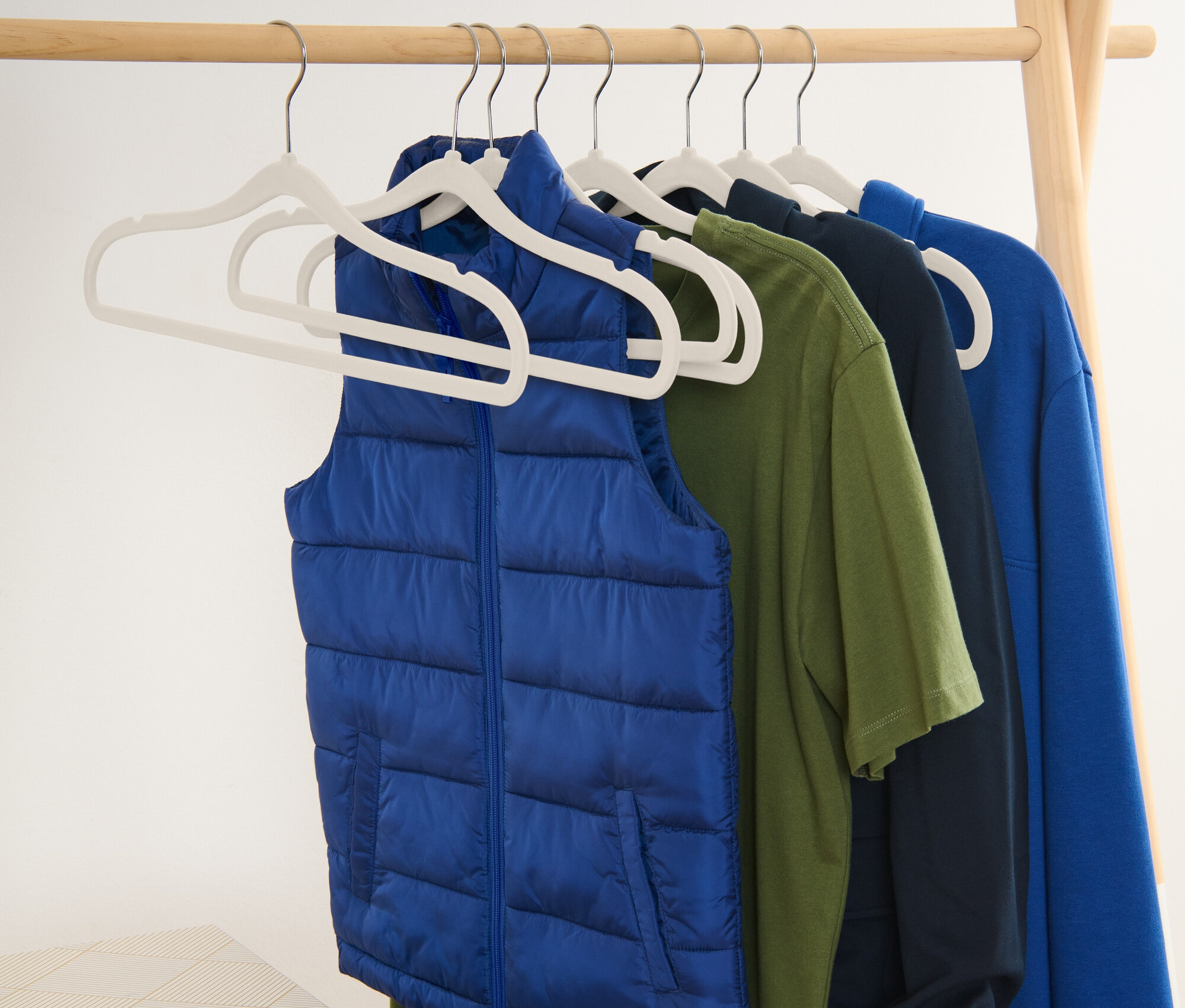Modrá vesta a trička visí na ramínkách na dřevěném stojanu.