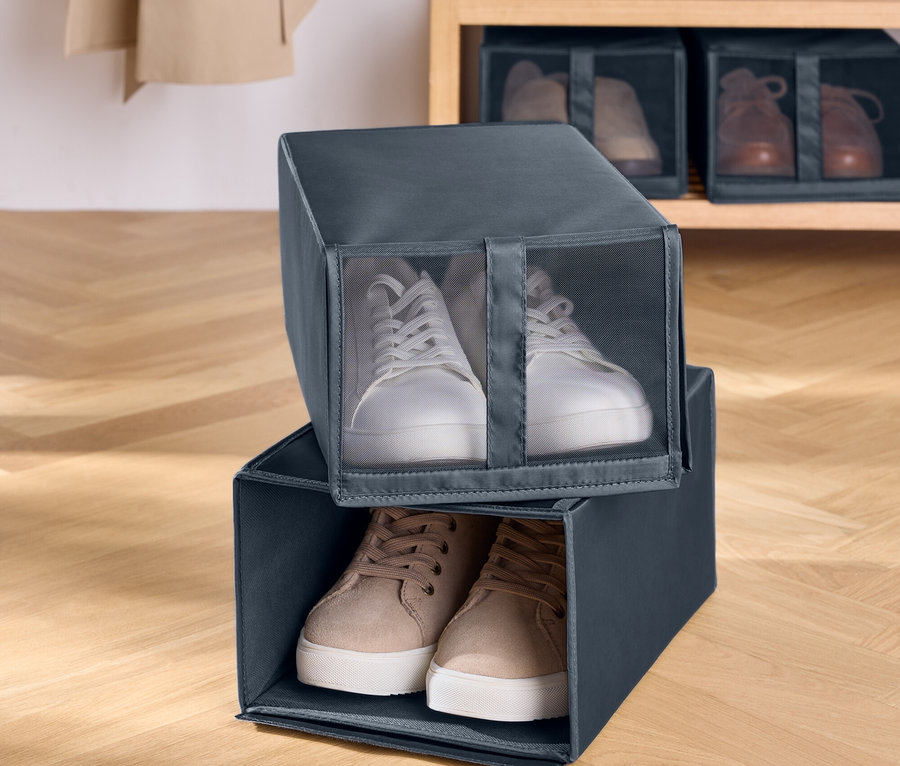 Dva šedé textilní boxy na boty naskládané na sobě. V horním boxu jsou bílé tenisky a ve spodním hnědé tenisky. V pozadí je dřevěný regál s botami.