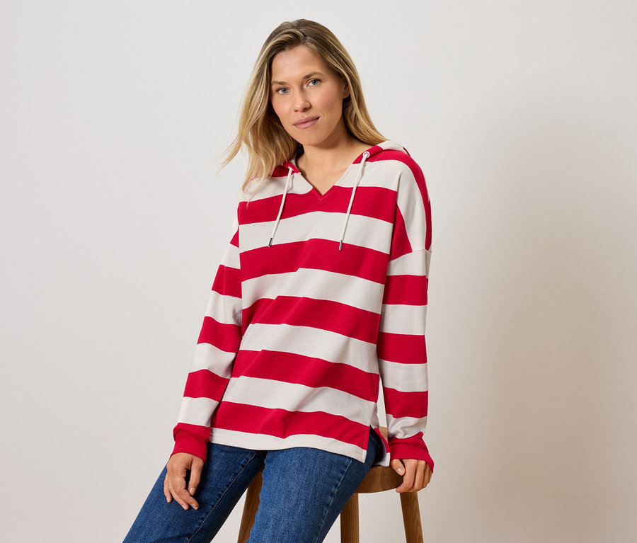 Žena sedí na stoličce a má na sobě pruhované tričko s kapucí a džíny.