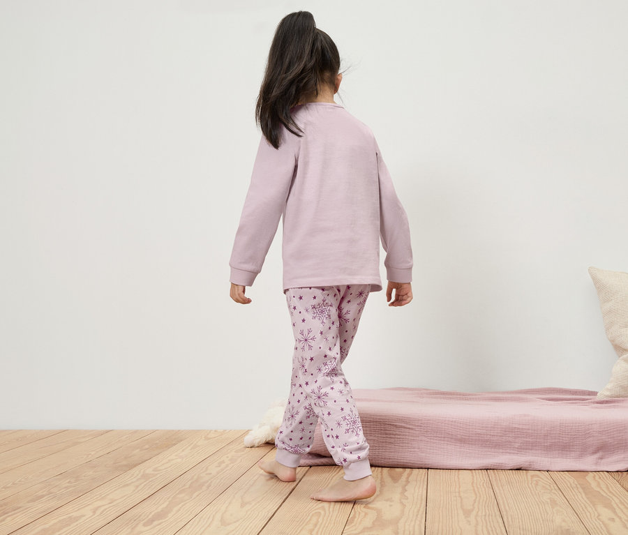 Dívka v pyžamu s dlouhým rukávem a sněhovými vločkami jde po dřevěné podlaze.