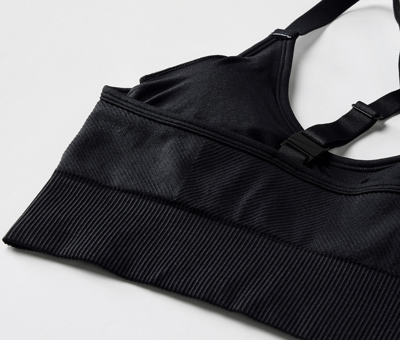 Detailní pohled na černou sportovní podprsenku s nastavitelnými ramínky a žebrovaným lemem.