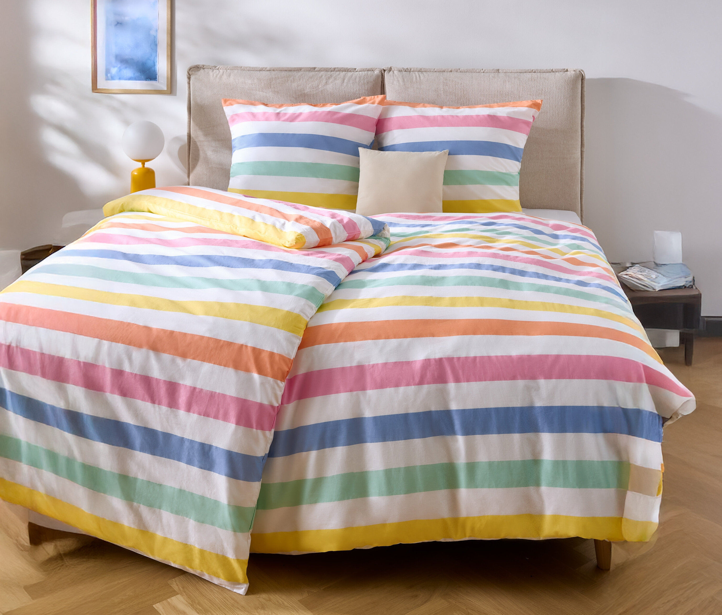 Postel s barevným pruhovaným ložním prádlem a dvěma polštáři.
