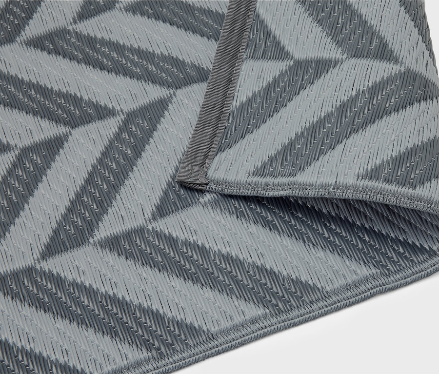 Šedá pikniková deka s geometrickým vzorem leží složená na bílém pozadí.