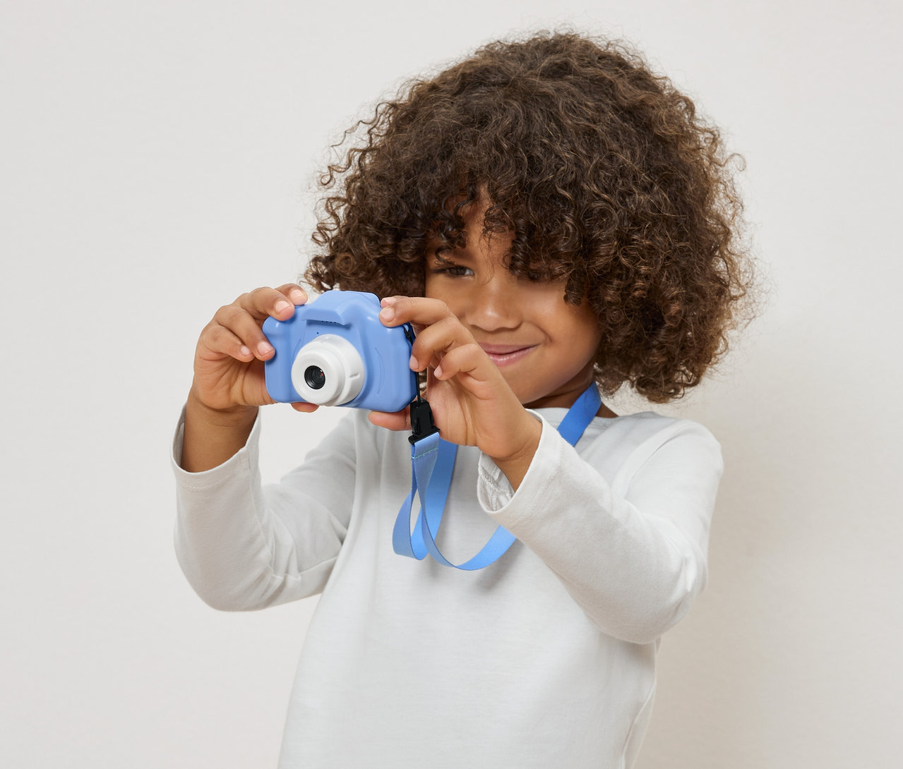 Dítě s kudrnatými vlasy drží modrý hračkový fotoaparát.