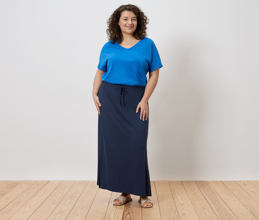 Žena má na sobě modré tričko a dlouhou, tmavě modrou sukni.