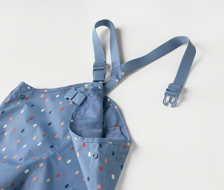 Modrá dětská zástěra s barevnými tečkami a modrými ramínky na bílém pozadí.