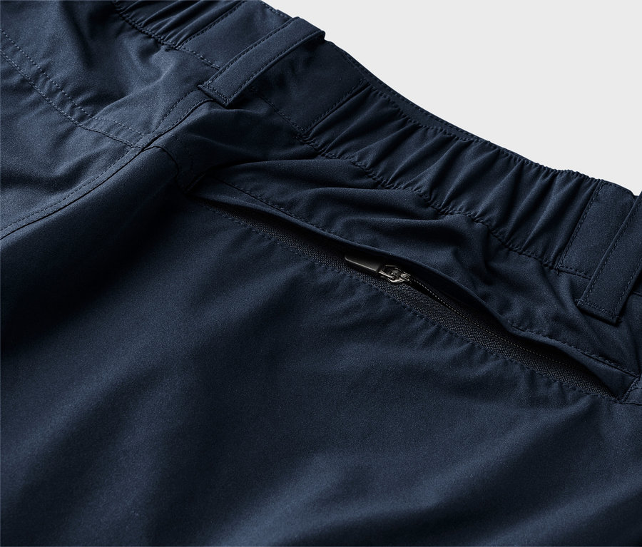 Detailní záběr na tmavě modré kalhoty s elastickým pasem a kapsou na zip.